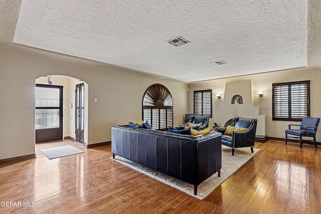 living area featuring arched walkways, a textured wall, a textured ceiling, hardwood / wood-style flooring, and visible vents