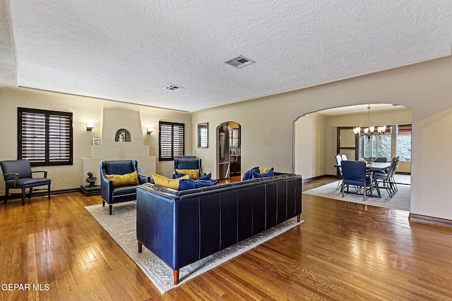 living area featuring visible vents, arched walkways, a textured wall, hardwood / wood-style floors, and an inviting chandelier