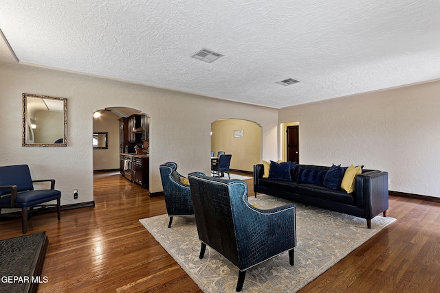 living room with arched walkways, a textured wall, and hardwood / wood-style floors