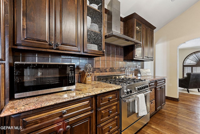 kitchen with arched walkways, wall chimney exhaust hood, dark brown cabinets, and high end range