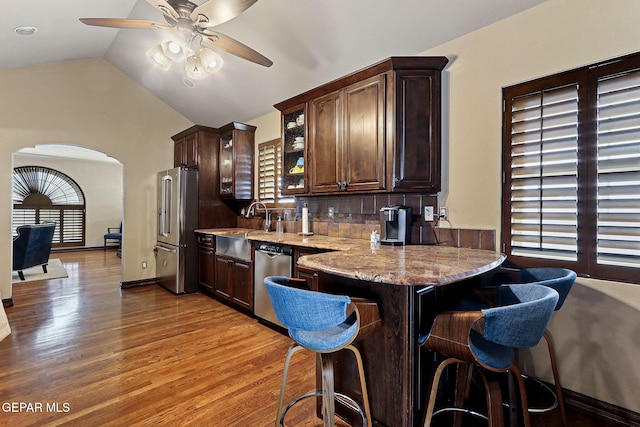 kitchen with a breakfast bar, lofted ceiling, appliances with stainless steel finishes, dark brown cabinetry, and wood finished floors