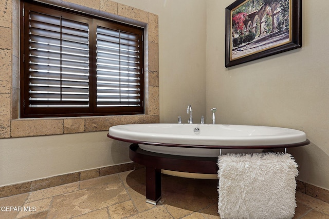 bathroom with stone tile flooring, a soaking tub, and baseboards