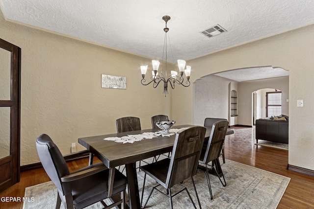 dining area featuring visible vents, arched walkways, wood finished floors, and a textured wall