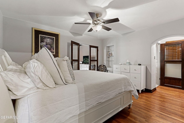 bedroom with arched walkways, ceiling fan, and wood finished floors