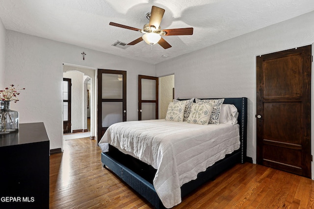 bedroom with visible vents, arched walkways, a textured wall, wood finished floors, and a textured ceiling