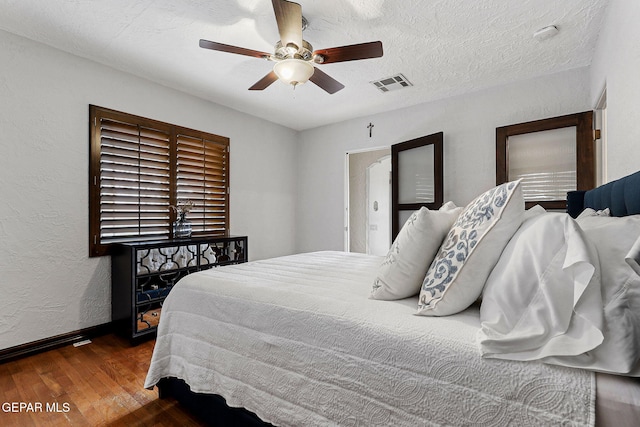 bedroom featuring a textured ceiling, a textured wall, ceiling fan, wood finished floors, and visible vents