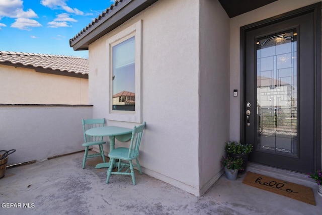 view of exterior entry with a tiled roof, a patio area, and stucco siding