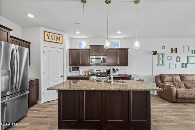 kitchen with light stone counters, stainless steel appliances, a sink, open floor plan, and tasteful backsplash