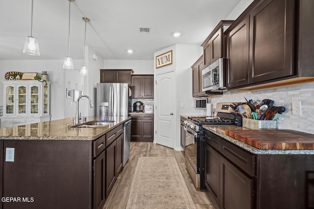 kitchen with stainless steel appliances, visible vents, a sink, dark brown cabinetry, and dark stone counters