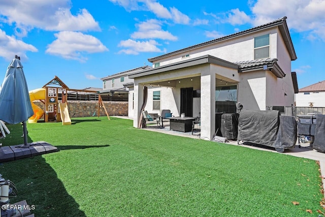 rear view of house with a patio, a playground, fence, a lawn, and stucco siding