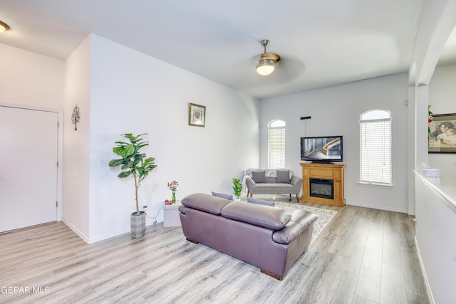 living area featuring light wood-style flooring, baseboards, and a glass covered fireplace