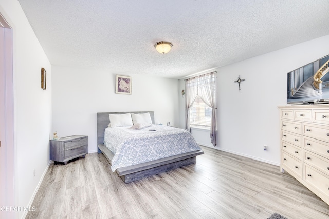 bedroom with light wood-style flooring, baseboards, and a textured ceiling