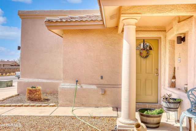 view of exterior entry with a tiled roof, visible vents, and stucco siding