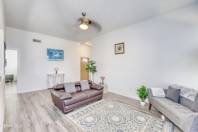 living room with visible vents, a textured ceiling, baseboards, and wood finished floors