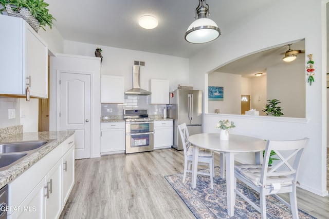 kitchen with appliances with stainless steel finishes, wall chimney range hood, light wood-style flooring, and white cabinetry