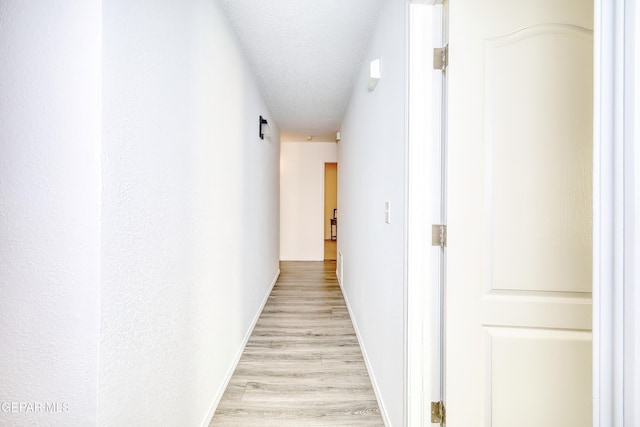 hall with light wood finished floors, baseboards, and a textured ceiling