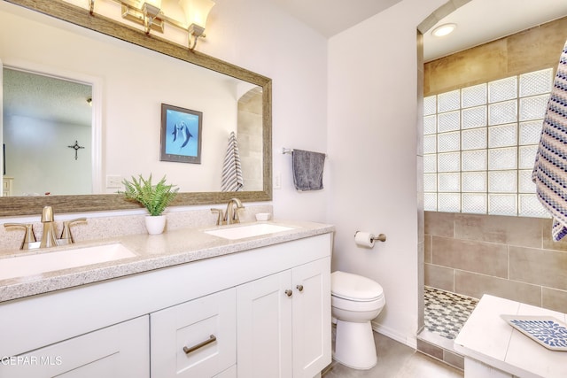 full bathroom featuring a sink, a tile shower, toilet, and double vanity