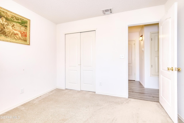 unfurnished bedroom featuring carpet, a textured ceiling, visible vents, and a closet