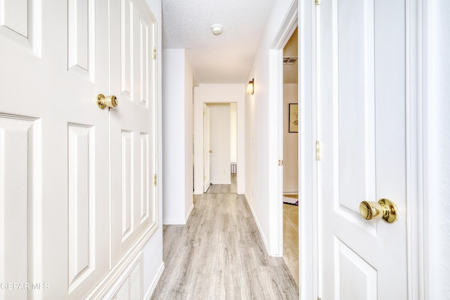 corridor with light wood-style floors, visible vents, baseboards, and a textured ceiling