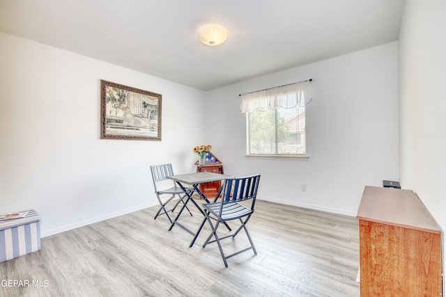 dining room featuring light wood-type flooring, baseboards, and a textured ceiling