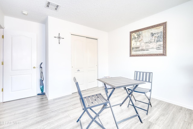 dining area featuring light wood-type flooring, visible vents, a textured ceiling, and baseboards