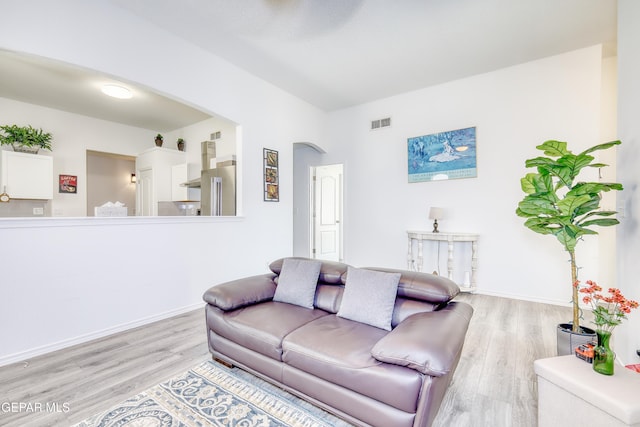 living area with light wood finished floors, visible vents, arched walkways, and baseboards