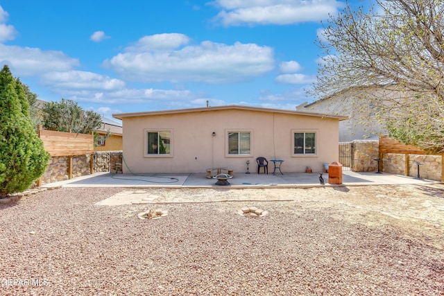 rear view of house featuring a patio area, a gate, fence, and stucco siding