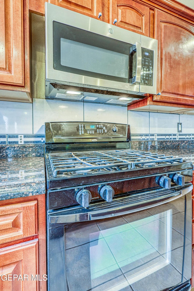 kitchen featuring gas stove, stainless steel microwave, brown cabinets, and dark countertops