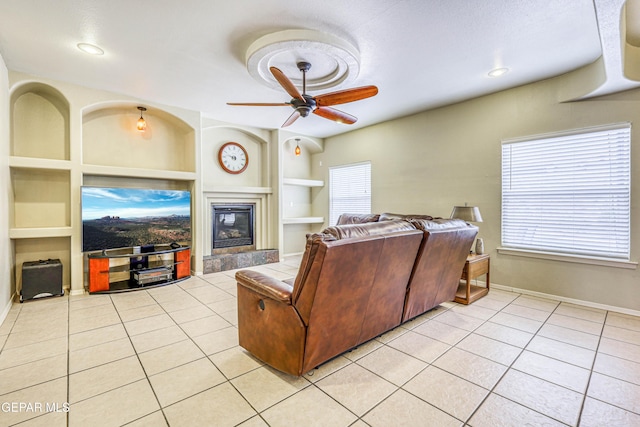 living room featuring light tile patterned flooring, built in shelves, a tiled fireplace, and a ceiling fan