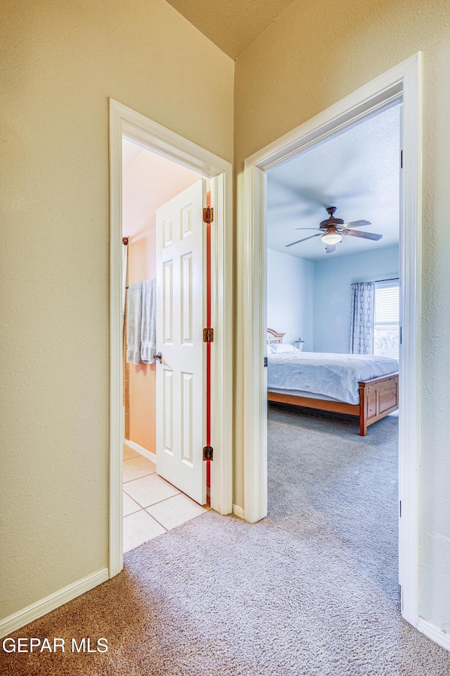 hallway featuring carpet flooring, baseboards, and a textured wall