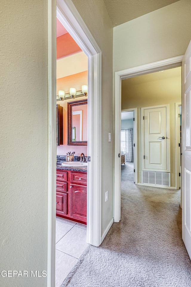 hall with a sink, visible vents, baseboards, and light colored carpet