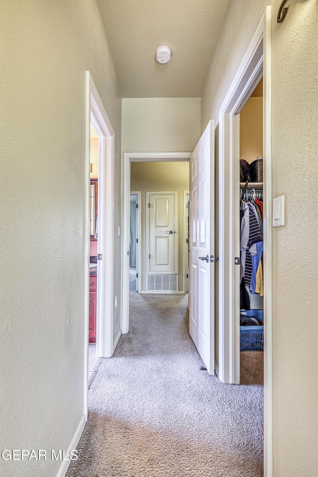 hall with visible vents, baseboards, carpet, and a textured wall