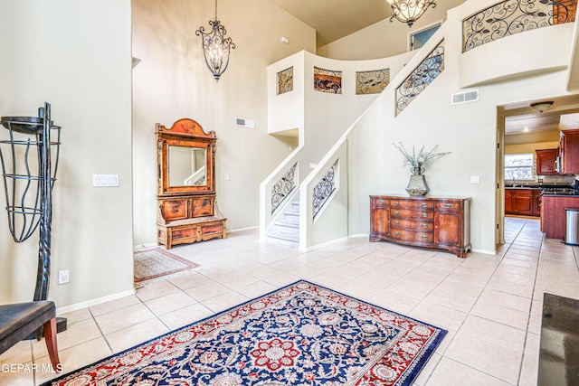 entryway with visible vents, stairs, light tile patterned floors, a high ceiling, and an inviting chandelier