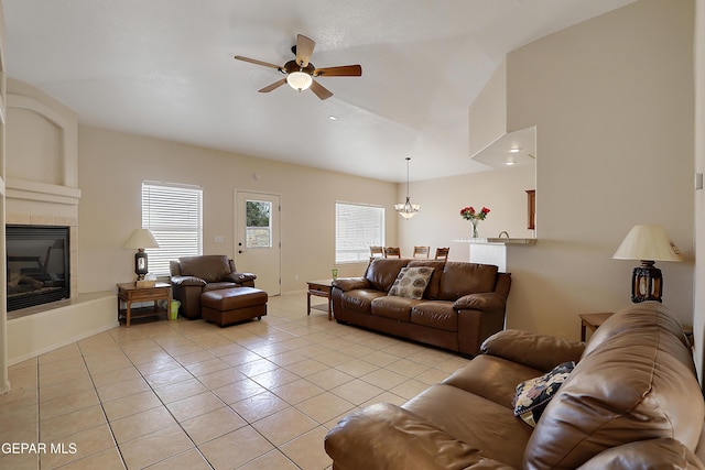 living room featuring a tile fireplace, light tile patterned flooring, lofted ceiling, and ceiling fan with notable chandelier