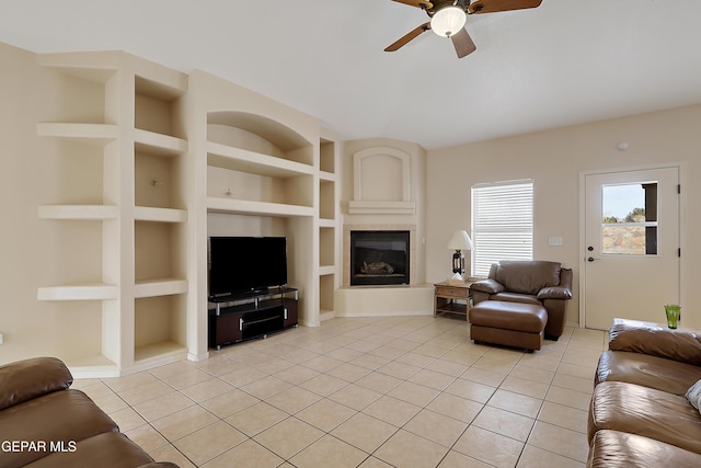 living area featuring built in shelves, a ceiling fan, a fireplace, and light tile patterned floors