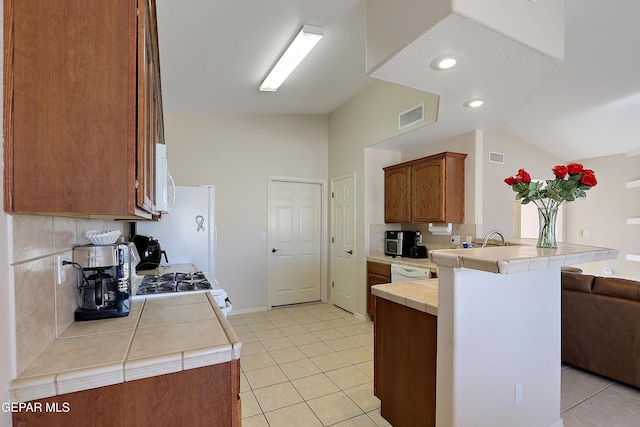 kitchen featuring lofted ceiling, tile countertops, a peninsula, visible vents, and decorative backsplash