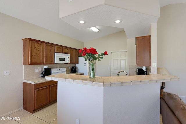 kitchen featuring a peninsula, white appliances, tile counters, and tasteful backsplash