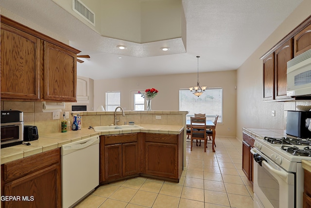 kitchen with tile countertops, white appliances, visible vents, and a sink