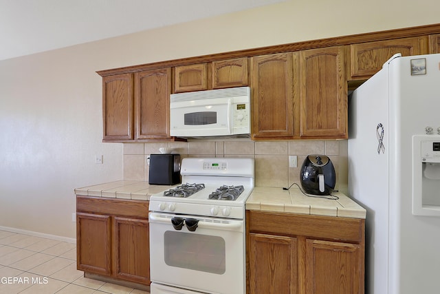 kitchen with brown cabinets, white appliances, tile counters, and decorative backsplash