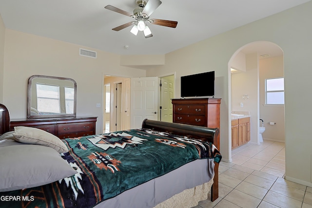 bedroom with arched walkways, visible vents, ensuite bathroom, light tile patterned flooring, and ceiling fan