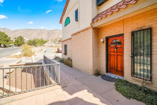 view of exterior entry with a tiled roof, brick siding, a mountain view, and stucco siding