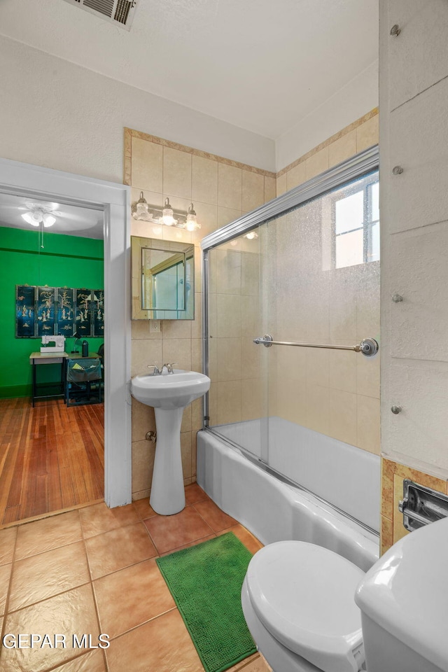 bathroom with visible vents, bath / shower combo with glass door, toilet, tile patterned floors, and tile walls