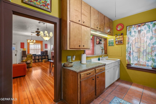 kitchen featuring brown cabinets, a notable chandelier, visible vents, light wood-style flooring, and a sink