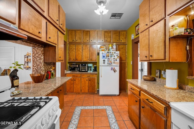 kitchen with light tile patterned floors, light countertops, visible vents, brown cabinetry, and white appliances