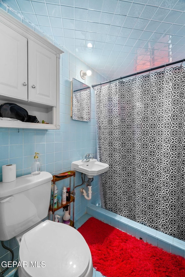 bathroom with toilet, a sink, tile walls, and a shower with shower curtain