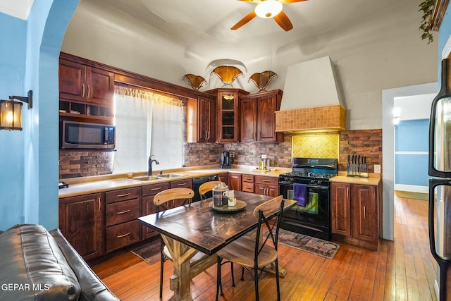 kitchen with dark wood finished floors, custom exhaust hood, stainless steel microwave, gas stove, and a sink