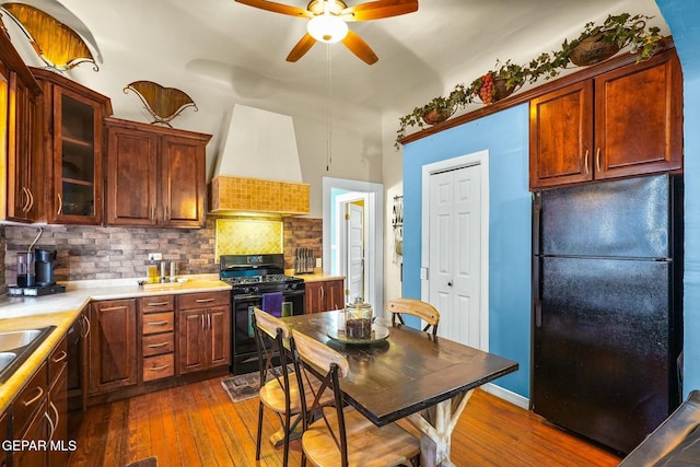 kitchen featuring dark wood-style flooring, custom range hood, decorative backsplash, ceiling fan, and black appliances