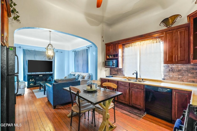 kitchen featuring arched walkways, a sink, black appliances, light wood finished floors, and tasteful backsplash