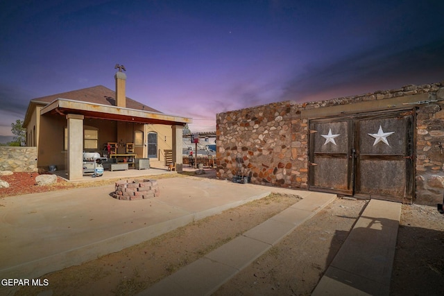 back of house featuring stone siding, a patio area, and a gate