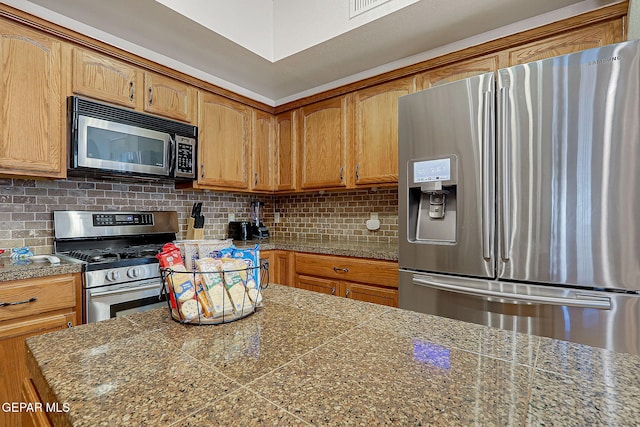 kitchen featuring appliances with stainless steel finishes, backsplash, tile counters, and brown cabinets